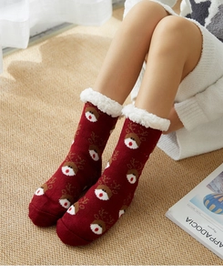 Detail of red Christmas socks with reindeer patterns and white plush cuffs on a mat