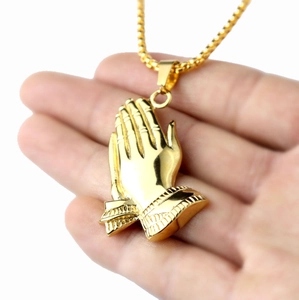 Golden stainless steel necklace featuring detailed praying hands pendant held in hand