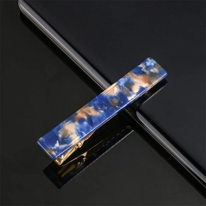 Detail of blue marble acrylic hair clip with gold metal alligator grip on black surface