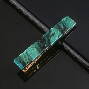 Macro detail of marbled dark green acetate hair clip with gold metal grip and sparkles