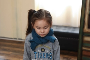 Detail view of blue ribbed knit scarf for children paired with a grey graphic sweatshirt