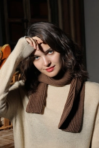 Close-up of a warm brown ribbed knit scarf styled on a model in a cozy indoor setting