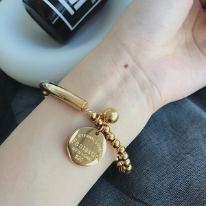 Detailed close-up of a gold bead bracelet featuring an engraved Eternal Love round charm