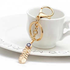 Golden feather keychain with blue evil eye bead detail leaning on a white ceramic cup