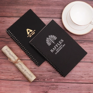 Detail of matte black spiral notebooks with custom gold foil logos on a wooden desk