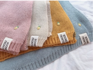 Détail d'écharpes tricotées en rose, beige, jaune et bleu avec petits décors d'ananas dorés
