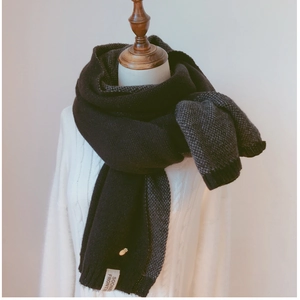 Détail d'une écharpe en maille noire avec broche ananas dorée et étiquette sur mannequin