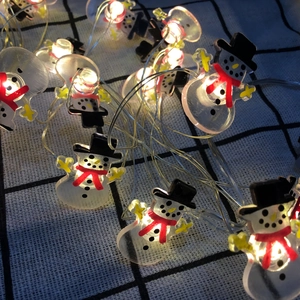 Close-up of LED snowman string lights with warm white glow on blue checkered fabric