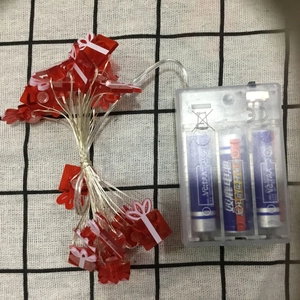 Detail of battery box and red gift box LED string lights on checkered fabric background