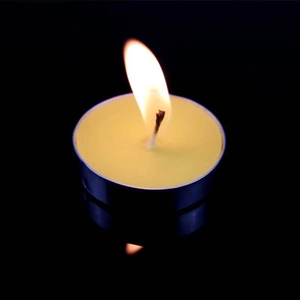 Yellow round tea light candle burning brightly with clear reflection on black background