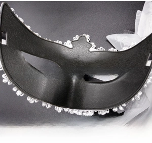 Close-up of black masquerade mask with white feather flower and delicate lace detail