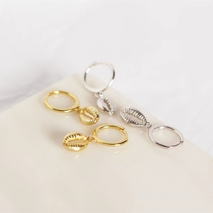 Detailed view of gold and silver shell drop earrings on a minimalist display stand