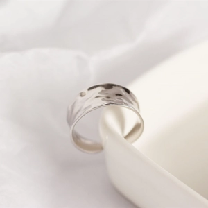 Macro shot of wide S925 sterling silver ring with irregular hammered texture on white fabric