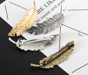 Detail of four metallic feather hair clips showing intricate textures and spring clasps