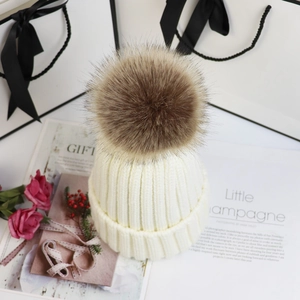 Nahaufnahme einer weißen Strickmütze mit einem flauschigen braunen Kunstfellbommel