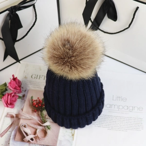 Detail einer dunkelblauen Strickmütze mit Kunstfell-Bommel in eleganter Geschenkbox