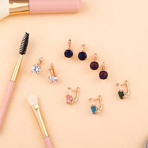 Détail de boucles d'oreilles en or rose avec zircons colorés à côté de pinceaux