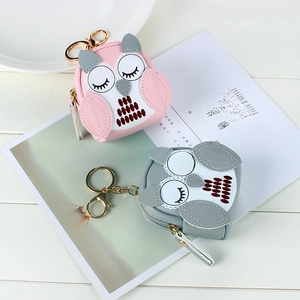 Close-up of pink and grey owl coin purses with gold keychains on a white table