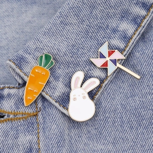 Close-up of enamel pin set with carrot, rabbit, and windmill on denim fabric