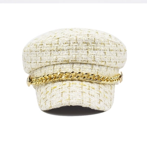 Detailed texture of white tweed newsboy hat with gold thread and chunky metal chain link