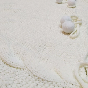 Detailed knit texture of white Christmas tree skirt with decorative pom-poms and drawstring