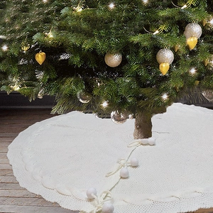 Detail of cable knit Christmas tree skirt with white pom-poms and decorative bow tie