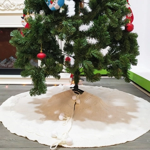 Detail of creamy white knitted Christmas tree skirt with decorative soft pom-pom ties