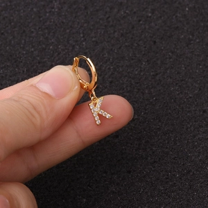Gros plan d'une boucle d'oreille dorée lettre K avec pierres de zircone sur l'oreille
