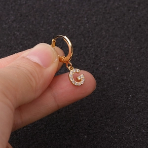 Vue macro de créoles dorées avec pendentif lettre G et oxydes de zirconium scintillants