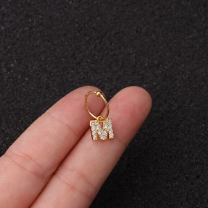 Gros plan d'une créole dorée avec pendentif lettre M en zircons, tenue par la main