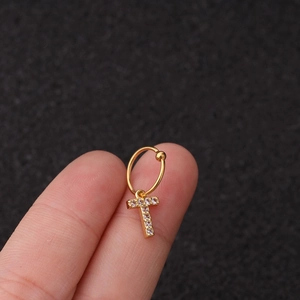 Détail d'un piercing d'oreille doré avec un pendentif en croix serti de zircons