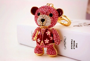 Detail of pink rhinestone bear keychain with red vest on a white book surface