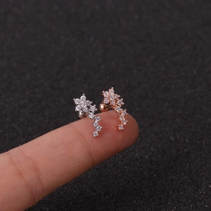 Macro view of silver and rose gold flower cartilage earrings with zircons on a finger