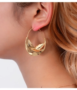 Close-up of a large irregular twisted leaf-shaped earring in a polished gold finish