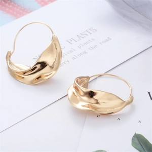 Minimalist gold hoop earrings with irregular lava texture shown on an artistic background