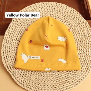 Detail of yellow cotton baby beanie with white polar bear print on a woven background