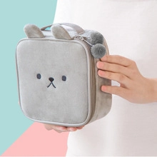 Close-up of grey plush storage bag featuring cute bear embroidery and fluffy pompom charms