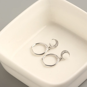 Detail of silver S925 crescent moon hoop earrings with cubic zirconia on white tray