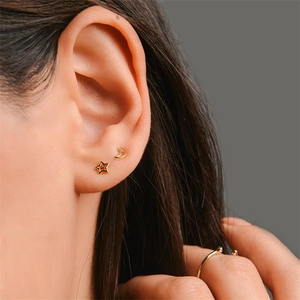 Macro shot of gold-plated crescent moon and star stud earrings worn on a female ear lobe