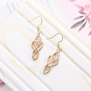 Detailed shot of golden hollow heart and infinity earrings on a white marble surface