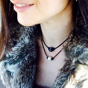 Detail of single black and white pearl necklaces on genuine leather cords worn by a model