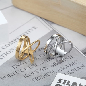 Modern gold and silver stainless steel X-shape crossover rings on a minimalist magazine