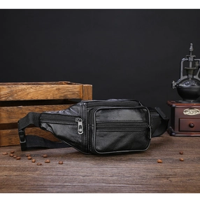 Detail of a vintage black leather fanny pack with multi-zipper pockets on a wooden desk