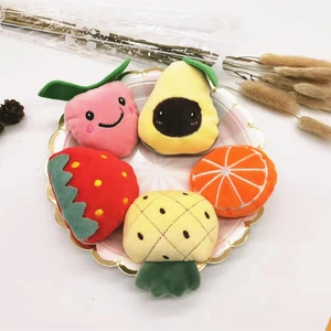 Detail of five cute plush fruit brooches including strawberry and avocado in a gold tray