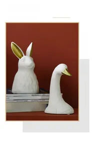 Detailed view of matte white ceramic rabbit vase with gold accents on modern books