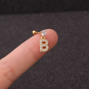 Macro view of a gold-plated letter B earring stud with zircon stones on a fingertip