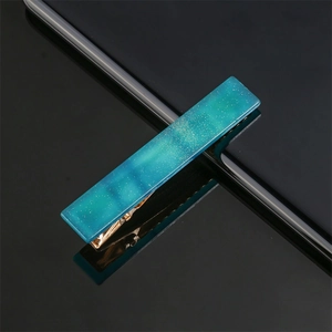 Close-up of blue-green resin bar hair clip with gold glitter and metal duckbill clamp
