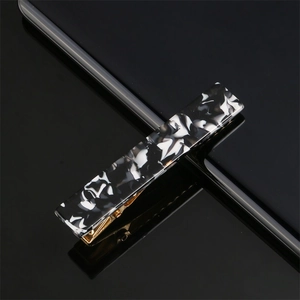 Close-up of a marbled acetate hair clip with black and white patterns on a mirror