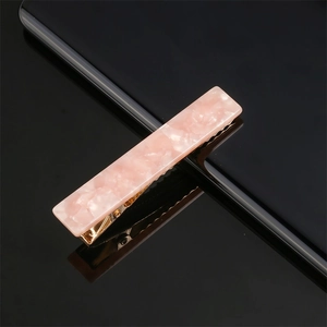 Close-up of pink marble pattern acetate hair clip with a golden metal base on black background
