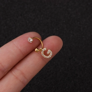 Vue macro d'un piercing de nombril doré lettre G incrusté de zircons étincelants